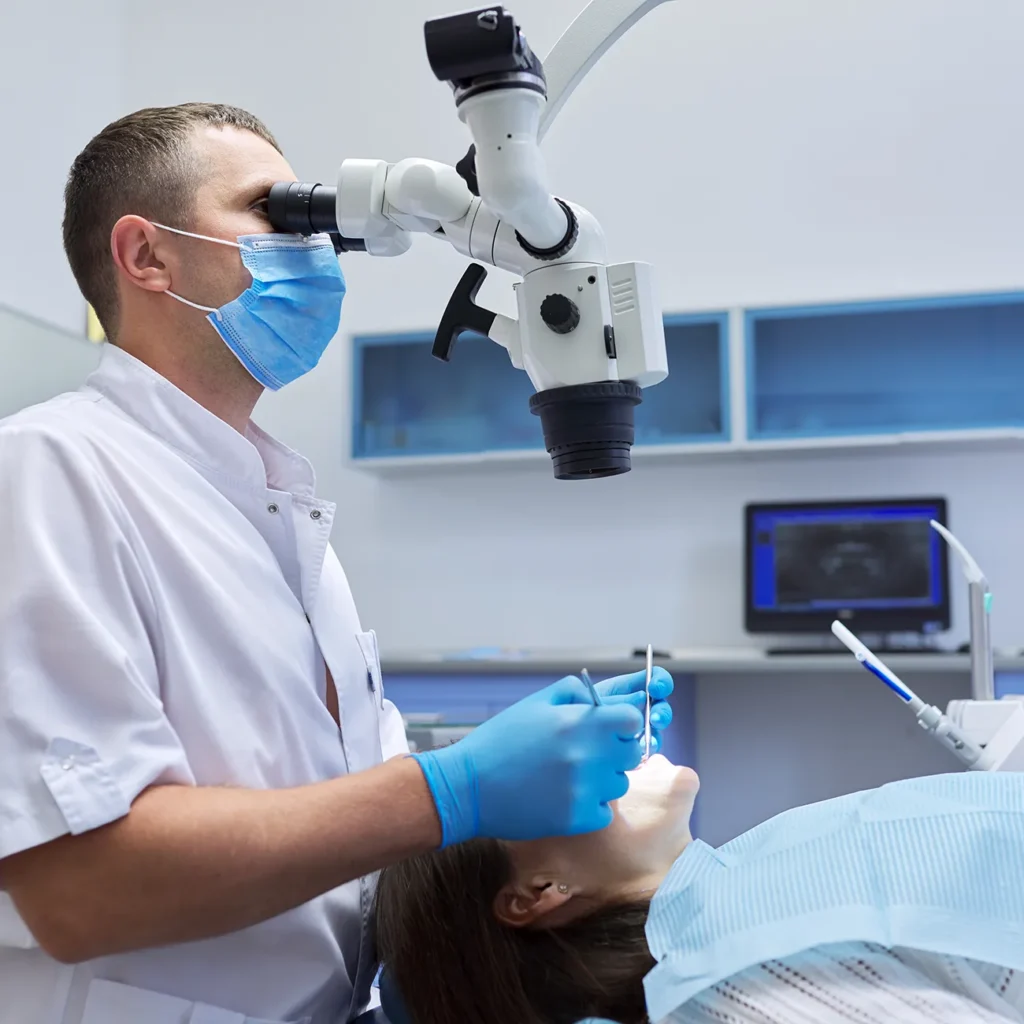 lekarz dentysta wykonuje zabieg endodontyczny pod mikroskopem